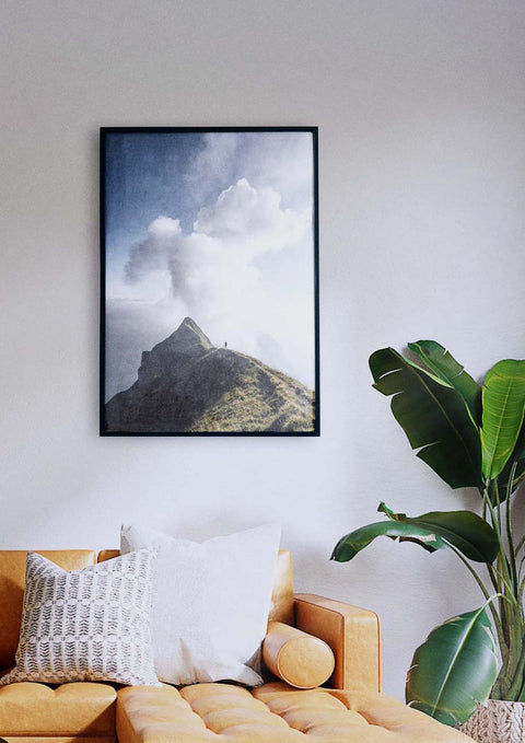 Über einer Couch im Wohnzimmer hängt ein Bild von Berg und Mann mit majestätischen Wolken.