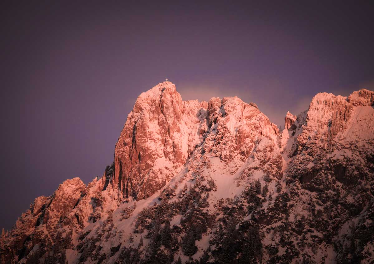 Bei Sonnenuntergang erstrahlen schneebedeckte Berggipfel in rosa und orangen Farbtönen.