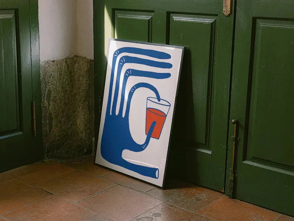 Ein gerahmtes Kunstwerk mit einer stilisierten blauen Hand, die eine rote Tasse hält, lehnt an einer grünen Tür auf einem gefliesten Boden.