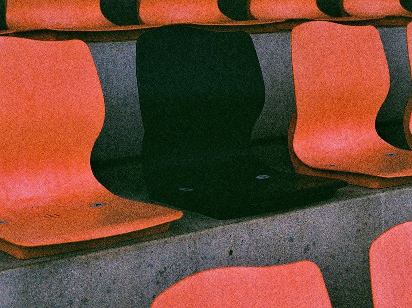 In einem Stadion wird ein schwarzer Sitz zwischen orangefarbenen Sitzen platziert.