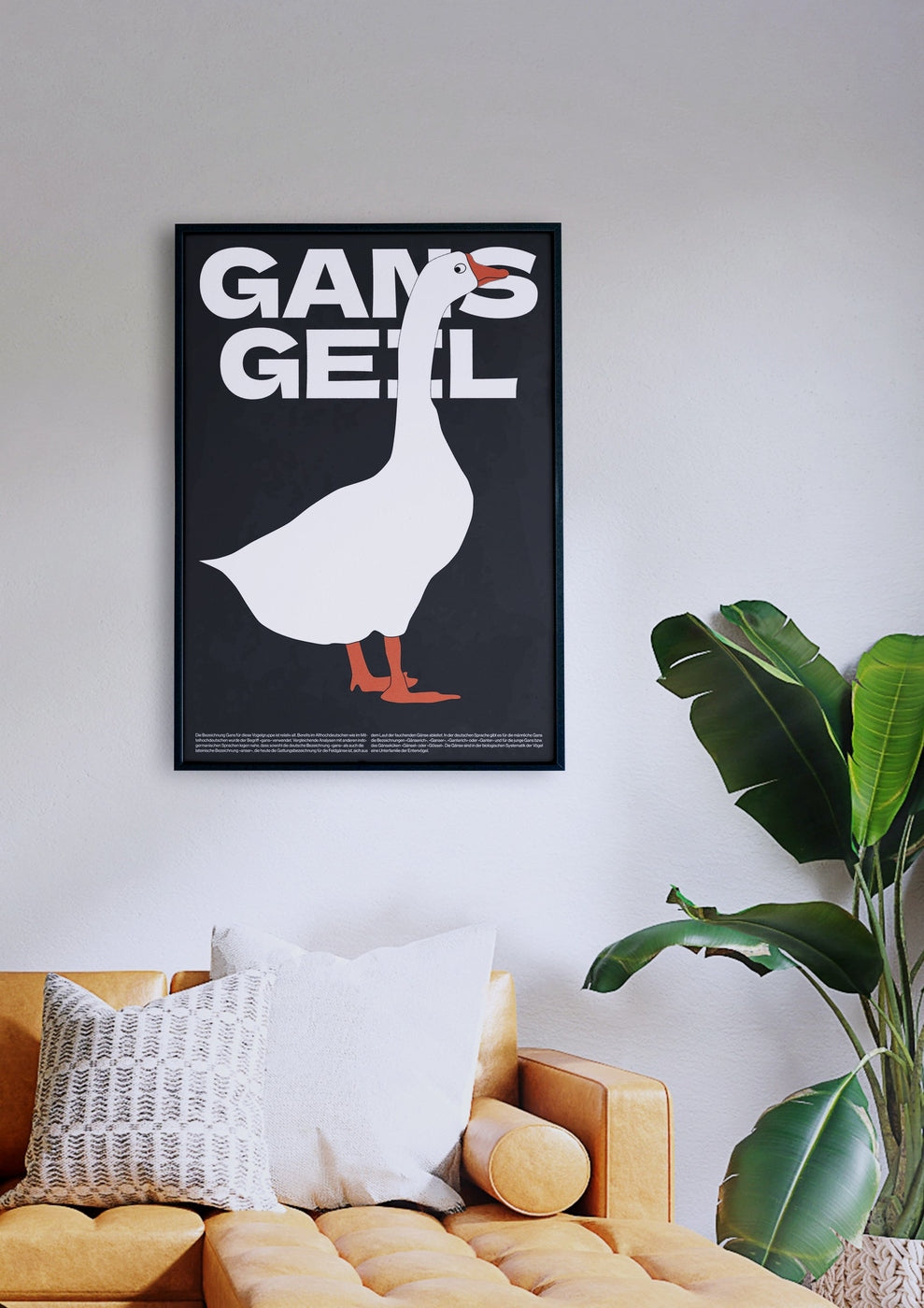 Das gerahmte Poster „Gans Geil“ mit einer weißen Gans und dem Text „GANS GEIL“ auf schwarzem Hintergrund hängt stilvoll über einer senffarbenen Couch mit weißen und gemusterten Kissen neben einer grünen Pflanze.