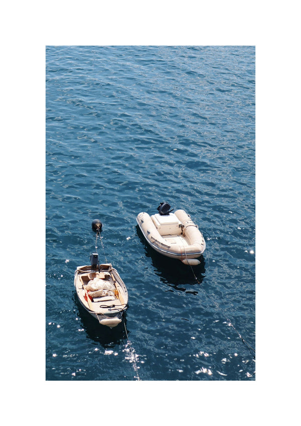 In „Mediterranean Meditation“ schwimmen zwei kleine Boote auf dem ruhigen blauen Wasser. Eines ist ein hölzernes Ruderboot mit Außenbordmotor, das andere ein Schlauchboot.