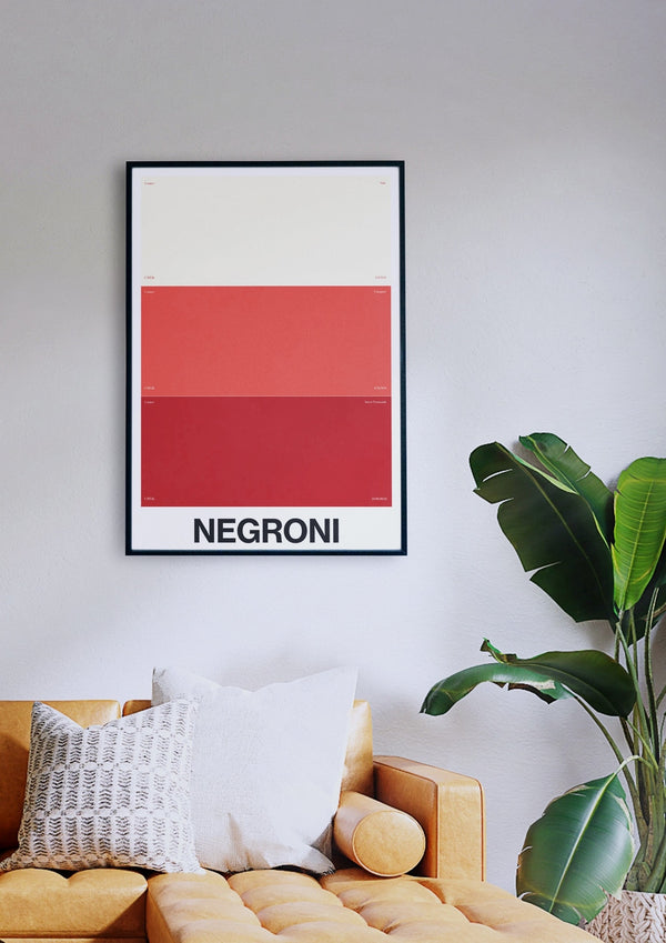 Das elegant gerahmte Farbverlaufsposter NEGRONI ziert eine weiße Wand über einem gelben Sofa, ergänzt durch ein weiß-graues Kissen und eine daneben stehende Topfpflanze.