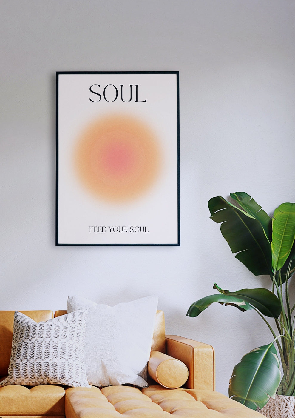 Das Wandbild „SOUL“ mit der Aufschrift „SOUL“ oben und „FEED YOUR SOUL“ unten in einem kreisförmigen Farbverlaufsdesign hängt elegant über einem hellbraunen Sofa mit grauen und weißen Kissen und einer daneben stehenden Topfpflanze.