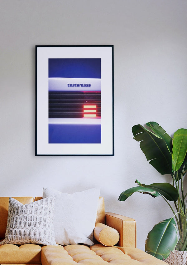 Das Kunstwerk „Testarossa“ im Retro-Design mit Text hängt an einer weißen Wand über einem senfgelben Sofa, auf dem ein gemustertes und ein weißes Kissen liegen. Neben dem Sofa steht eine grüne Pflanze.