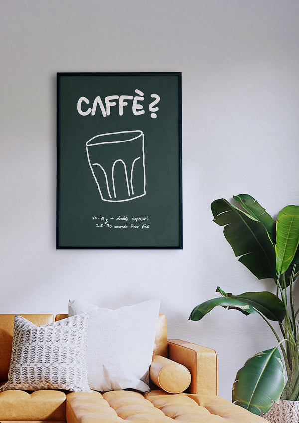 Ein gerahmter Druck mit dem Titel „Caffè? (Grün)“ mit dem Text „CAFFÈ?“ und einer skizzierten Kaffeetasse, der über einem senfgelben Sofa mit weißen und gemusterten Kissen neben einer grünen Pflanze hängt.