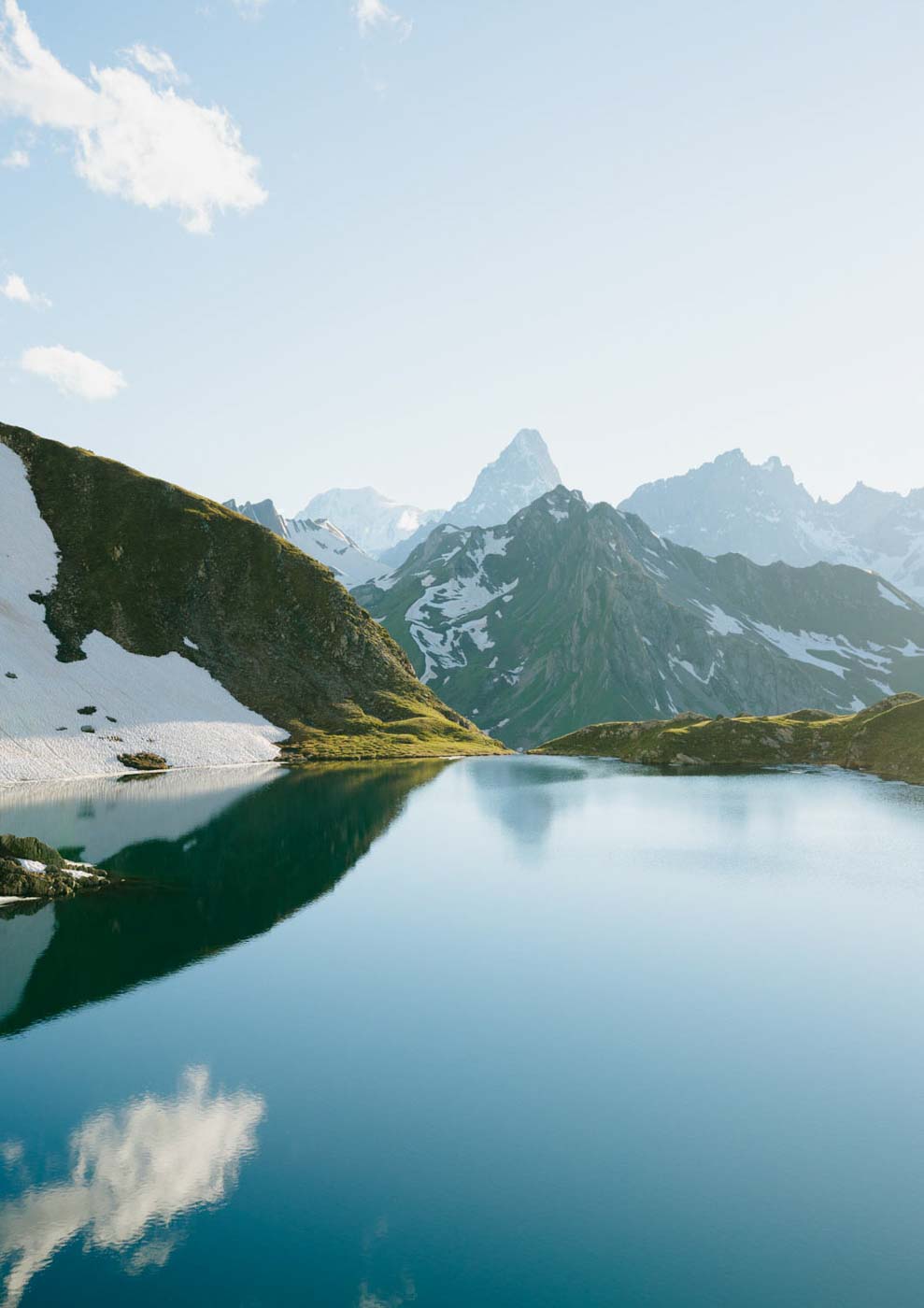 Ein Bergsee in der alpinen Landschaft mit schneebedeckten Bergen im Hintergrund.