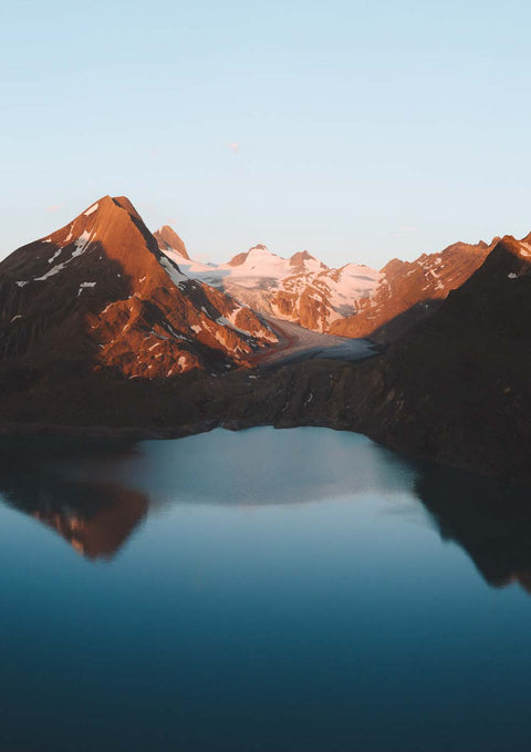 Eine Luftaufnahme eines Sees mit Bergen im Hintergrund und einem gletscherblauen Sonnenuntergang.