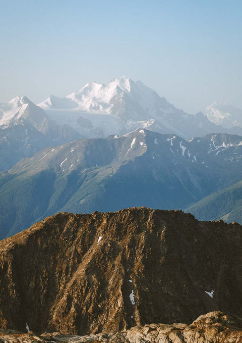 Ein Mann steht auf einem Gipfel mit einer Natur-Gebirgslandschaft und schneebedeckten Bergen im Hintergrund der Mittagssicht.