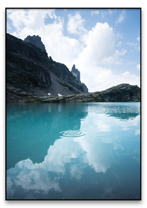 Ein blauer Spiegelsee umgeben von Bergen und Wolken.