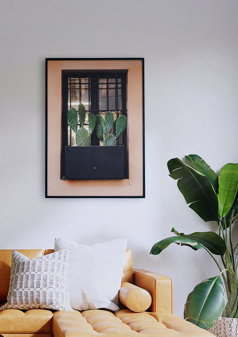 Ein Wohnzimmer mit einem Sofa ohne Rückgrat und einem gerahmten Foto eines Kaktus im Fenster.