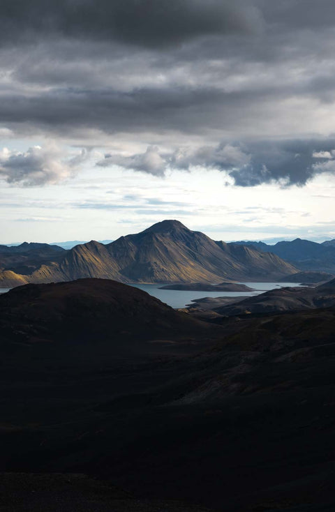 Ein dunkler Wolkenaufzug über einer Berglandschaft mit einem See im Hintergrund.